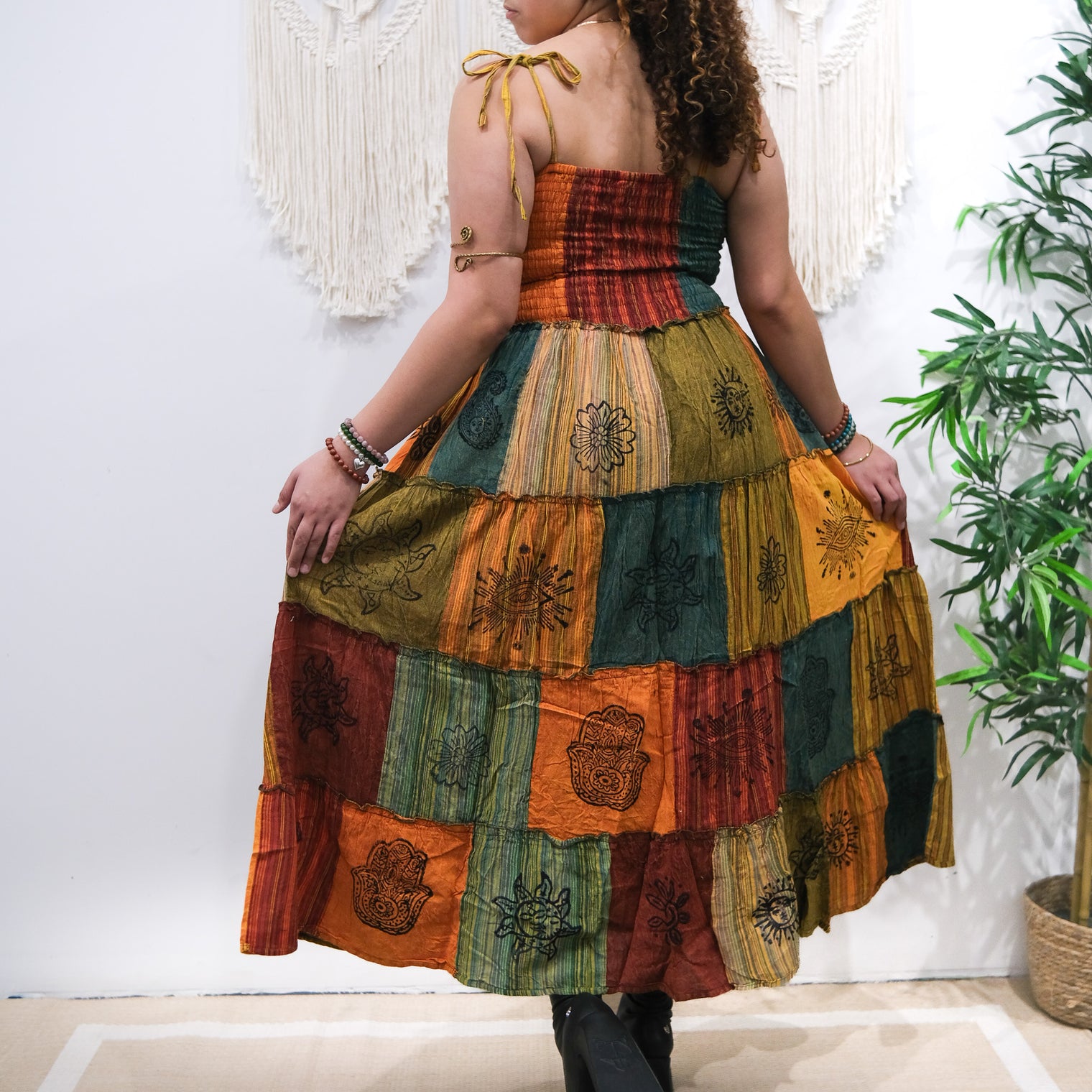 Woman wearing a colorful patchwork dress with a plant in the background